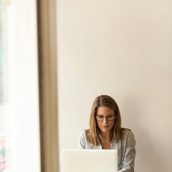 Businesswoman working remotely on a laptop at home, enjoying natural light in a modern, minimalist setting.