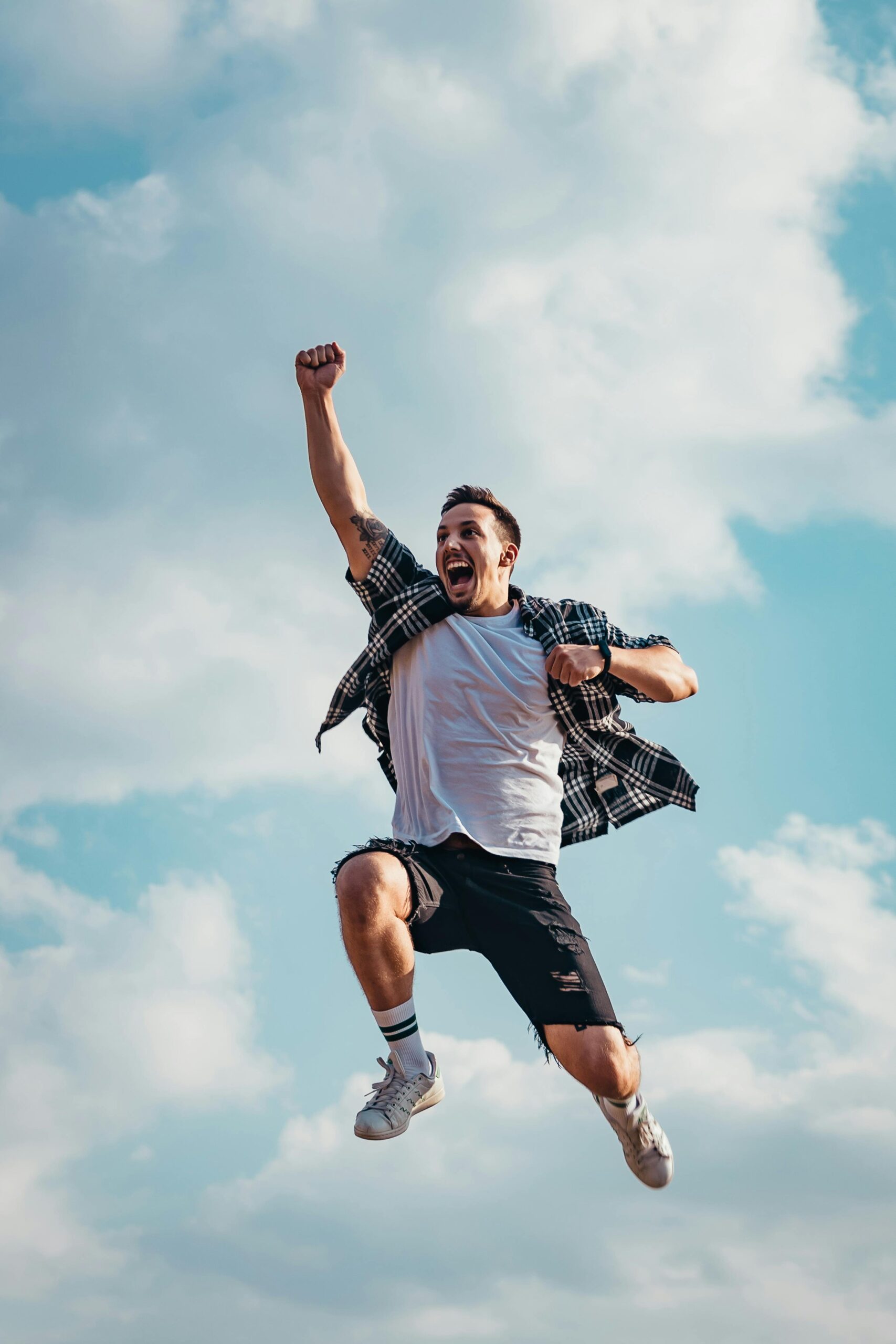 A joyful young man jumps midair with clouds and blue sky in the background, exuding energy and freedom.