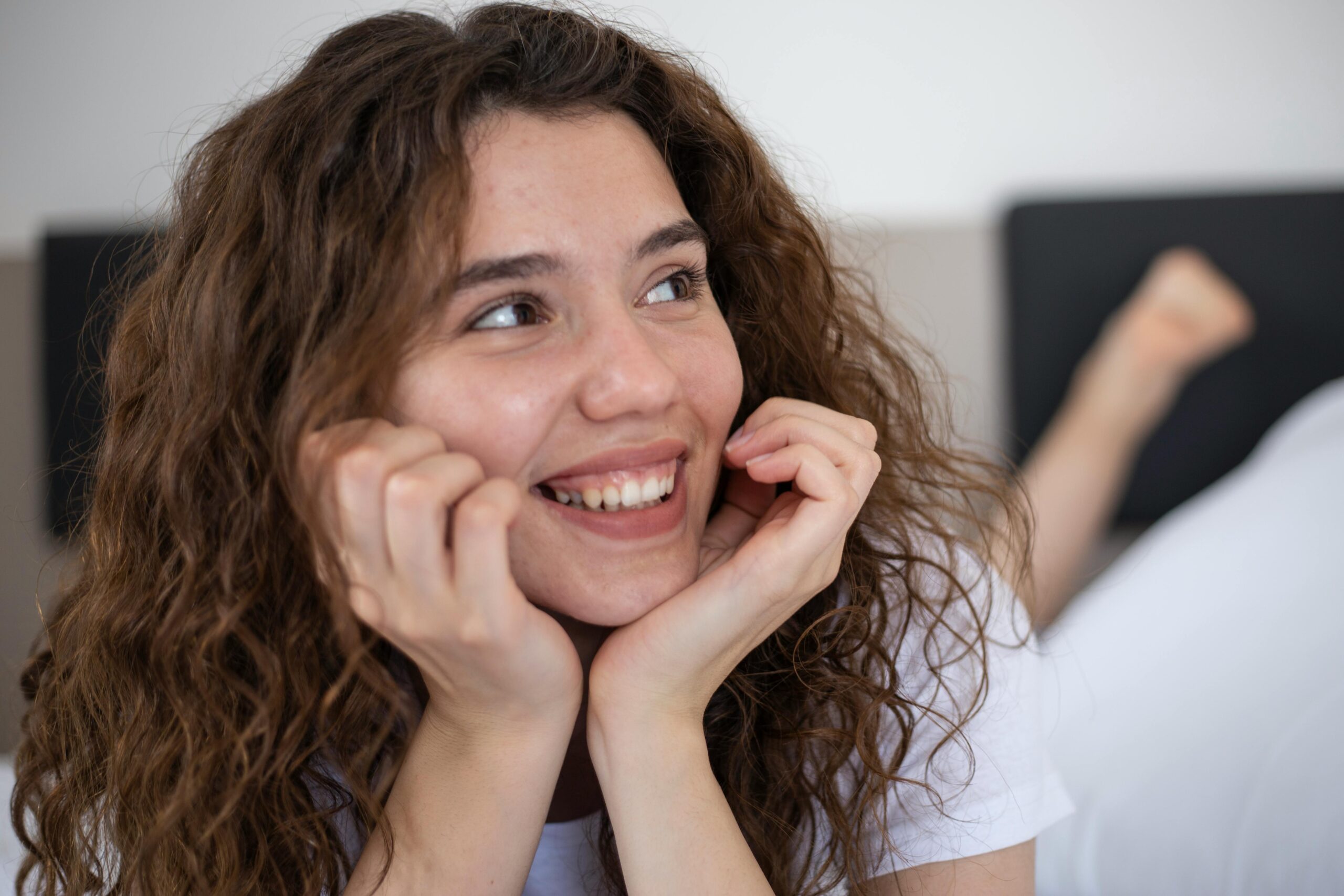 Close-up of a smiling woman with curly hair relaxing indoors, expressing joy and contentment.