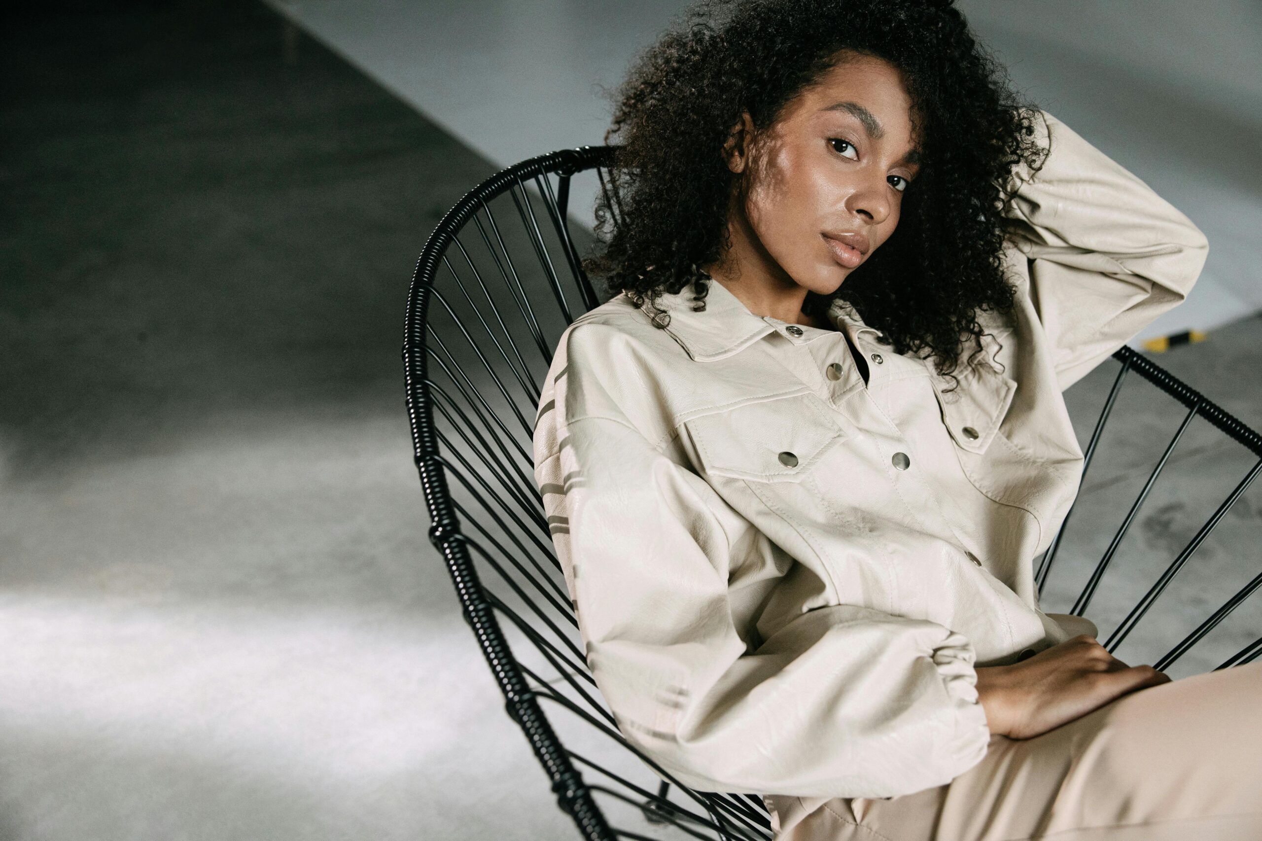 Portrait of a stylish woman posing on a metal chair in a minimalist setting, conveying modern elegance.